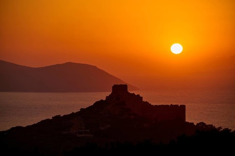 Castle ruins in silhouette against a dramatic sunset over the sea and mountains, Kritinia Castle,