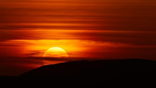 A dramatic sunset behind a hill that bathes the sky in deep red-orange tones, offshore island,