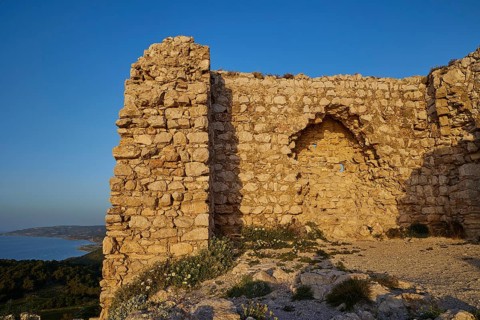 A historic stone ruin on a hill overlooking the sea and vegetation, Kritinia Castle, St John's