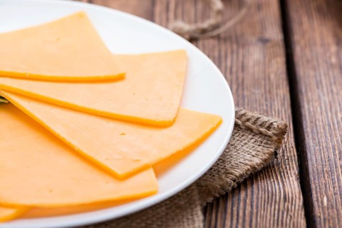 Portion of Cheddar Slices on wooden background (close-up shot)