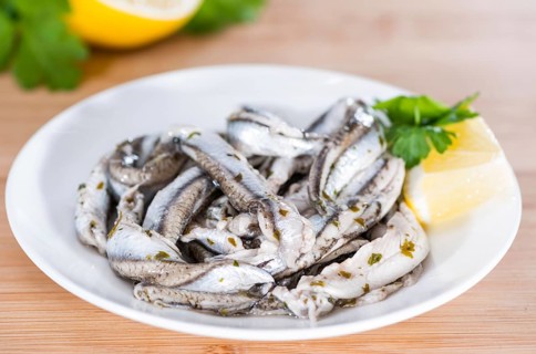Pickled Anchovis with herbs (close-up shot) on wooden background
