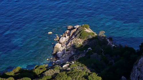 View from above of the rocky coastline where the blue sea meets the cliffs, surrounded by green