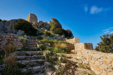 Stone steps lead to the ruins of an ancient castle, surrounded by nature under a blue sky, Kritinia