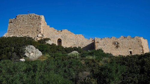 Ruins of an old building under a clear blue sky, surrounded by green overgrown grounds, Kritinia