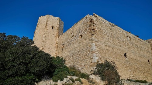 Corner of a castle ruin with massive stone tower, sparse vegetation, under a clear blue sky,