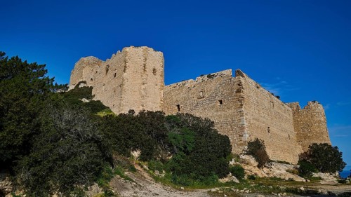 Ruins of a large castle complex, surrounded by dense vegetation and a clear blue sky, Kritinia