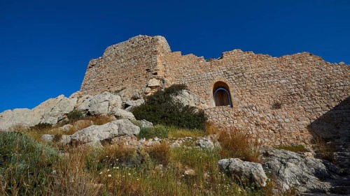 Ruins of a castle with partially preserved walls and a window, surrounded by vegetation under a