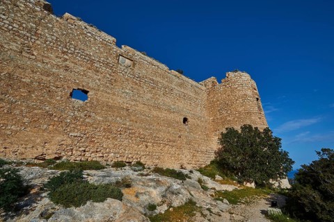 Side view of an old castle with thick stone walls and sparse vegetation under a clear sky, Kritinia