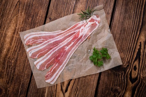 Portion of raw Bacon (close-up shot) on wooden background