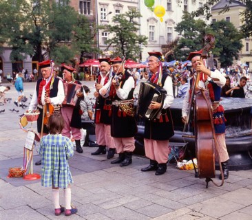 Little girl listens to music band of elderly men dressed in Polish national costumes in a square in