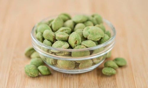 Wasabi coated Peanuts as high detailed close-up shot on a vintage wooden table (selective focus)