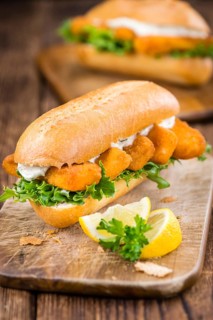 Roll with fried Fish Sticks (close-up shot) on an old wooden table