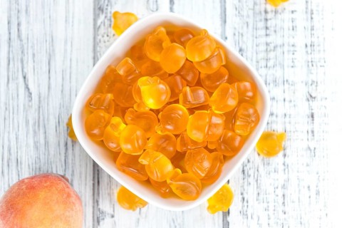 Gummy Peaches (close-up shot) with some fresh fruits on wooden background