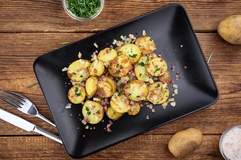 Fried Potatoes with Onions ond ham on a wooden table (selective focus)