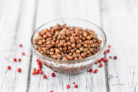 Preserved Pink Peppercorns on an old wooden table as detailed close-up shot, selective focus
