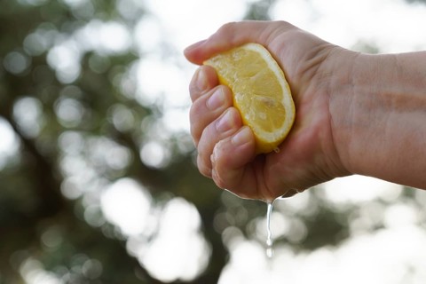 Woman squeezes a lemon with her hands the juice falls into a glass bowl, in the background is a