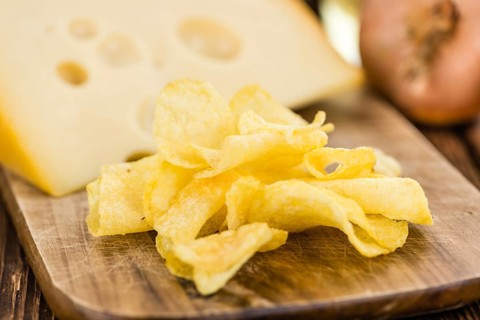 Cheese and Onion Potato Chips on an old wooden table as detailed close-up shot (selective focus)