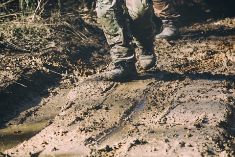 Brown military boots on mud, dirt and puddle