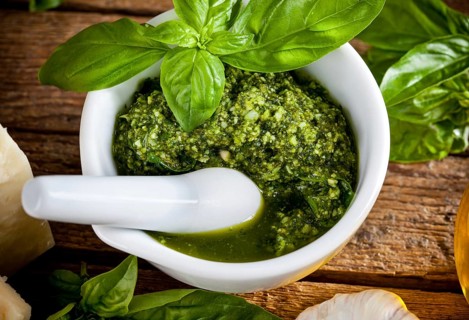 Homemade pesto sauce with basil and pine nuts in white mortar over old wooden table