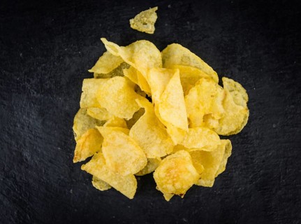 Portion of Cheese and Onion Potato Chips as detailed close up shot on a slate slab (selective