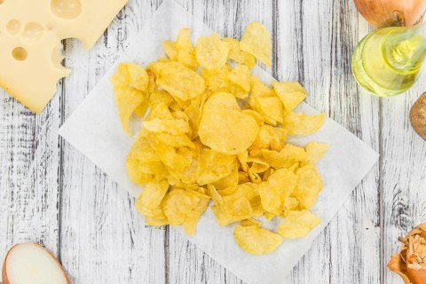 Cheese and Onion Potato Chips on an old wooden table as detailed close-up shot (selective focus)
