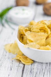 Potato Chips (Sour Cream taste) on a vintage background as detailed close-up shot (selective focus)