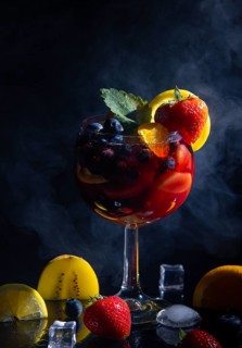 Fruity cocktail in a wine glass, with fresh strawberries, blueberries and oranges, against a dark
