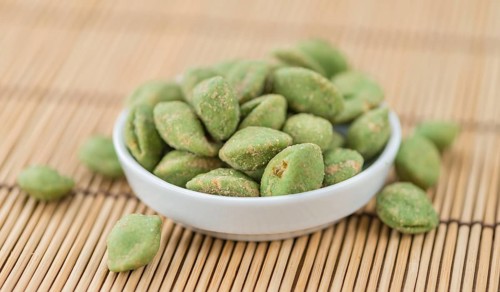 Wasabi coated Peanuts as high detailed close-up shot on a vintage wooden table (selective focus)