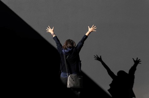 Woman Standing with Arms Raised Against a Grey Wall with Diagonal Shadow in a Sunny Day in