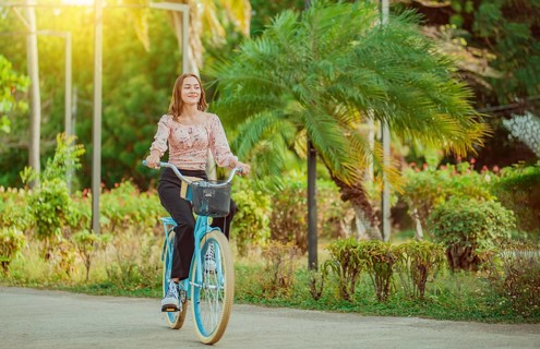 Beautiful and smiling young woman riding a bicycle in a nice park, looking at camera. Cheerful