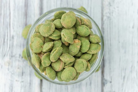 Wasabi coated Peanuts as high detailed close-up shot on a vintage wooden table (selective focus)