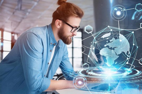 A man in a modern office works on a laptop with a holographic globe and technological graphics in
