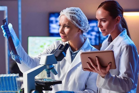 Two lab assistants analyse samples, one at the microscope, the other with a tablet, AI and