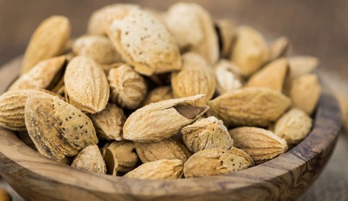 An old wooden table with roasted Almonds (in the shell) as detailed close-up shot (selective focus)
