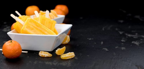 Homemade Tangerine Popsicles with some fresh fruits (close-up shot) on a vintage background