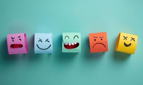 A row of paper cutouts of different emotions, including a smiley face and a frowning face AI