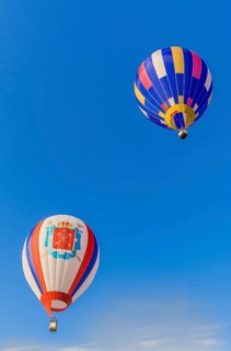 Two colorful hot air balloons with striped patterns floating in a clear blue sky, Belarus, Minsk,