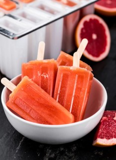 Some homemade Grapefruit Popsicles (with some fresh fruits) as close-up shot (selective focus)