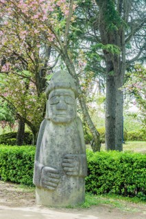 A large stone statue in a garden area with trees and bushes, in Suncheon, South Korea, Asia