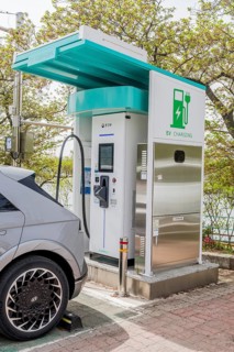 Electric vehicle charging station with a car connected, under a canopy surrounded by greenery, in