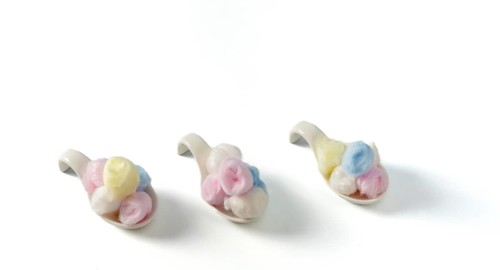 Cotton balls of different colors on white ceramic spoons on a white background