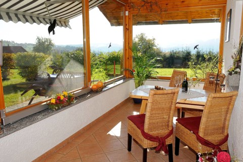 Cosy conservatory as a dining area with wooden table and chairs, surrounded by windows with views