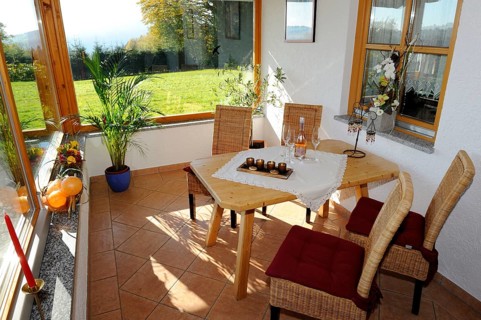 Cosy conservatory as a dining area with wooden table and chairs, surrounded by windows with views
