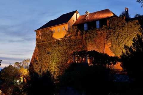 An illuminated castle at dusk with ivy-covered walls on a hill, Stallbastei, Schlossberg, Graz