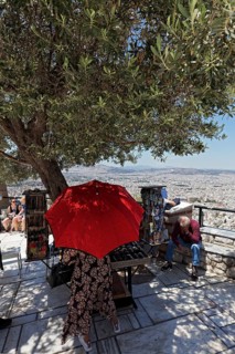 Souvenir stand under a shady olive tree, woman with parasol, panoramic terrace on Lycabettus Hill,