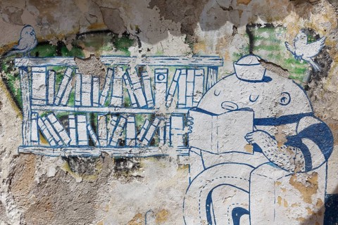 Reading figure in front of a bookshelf, weathered graffiti, street art in the Plaka neighbourhood,