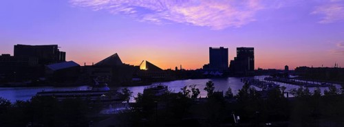 A dramatic and beautiful panoramic sunrise with buildings and boats in silhouette reflected in the
