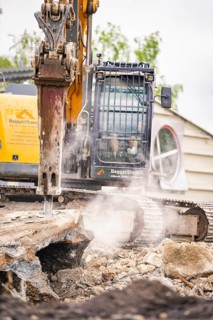 An excavator on a construction site tears down concrete blocks, dust rises, demolition site,