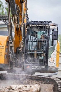Excavator during demolition, breaking up concrete. The driver is visible in the cab, demolition