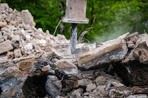 Excavator breaks up concrete and rubble and dust can be seen on a construction site, Demolition